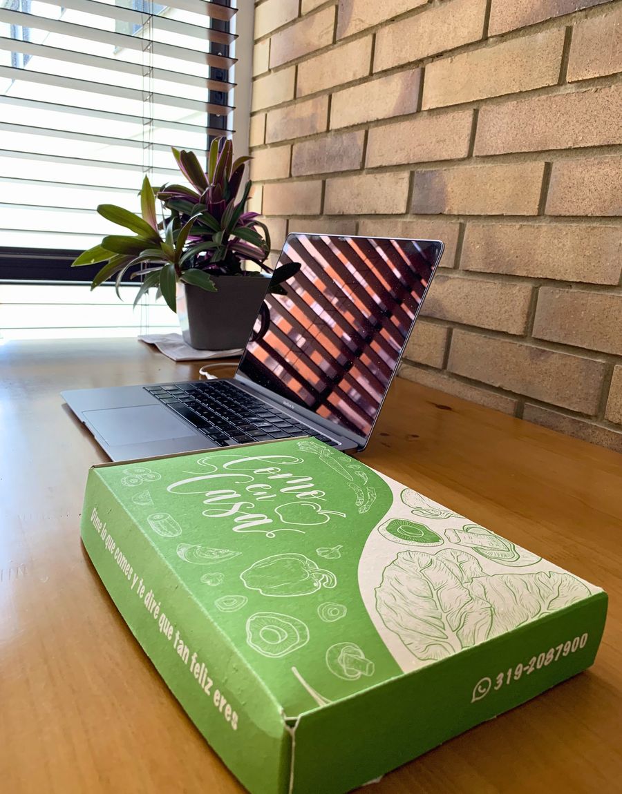 Caja de almuerzo Como en Casa entregada en el escritorio de la oficina, junto a un portátil y una planta